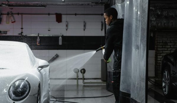 Man in Black Jacket Washing the White Car Using a Washer Pressure Hose